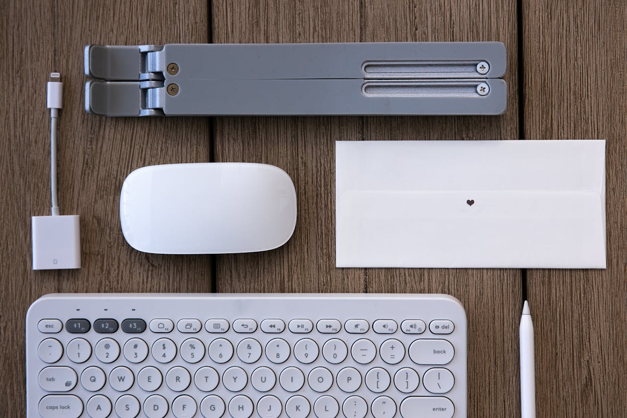Flat lay of modern tech peripherals and stationery on a wooden desk.